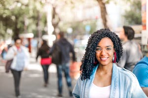 Confident woman smiling on a sunny day amidst a bustling urban street scene.